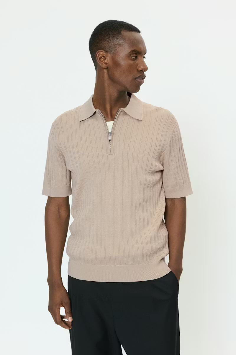 Tämä ribbineulos-polo yhdistää klassisen ilmeen ja modernin viimeistelyn. Puolivetoketju edessä ja siisti kaulus luovat raikkaan ja huolitellun siluetin, kun taas lyhyet hihat ja vartalonmyötäinen malli tuovat asuun trendikästä ilmettä.