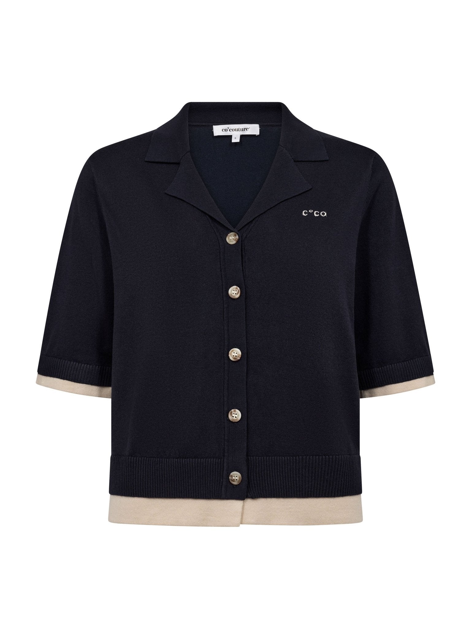 Co’Couture LueCC Crop Cardigan on lyhyt tummansininen neuletakki, jossa on kaulus, lyhyet hihat ja nappikiinnitys. Väljä malli sopii helposti kerrostamiseen.