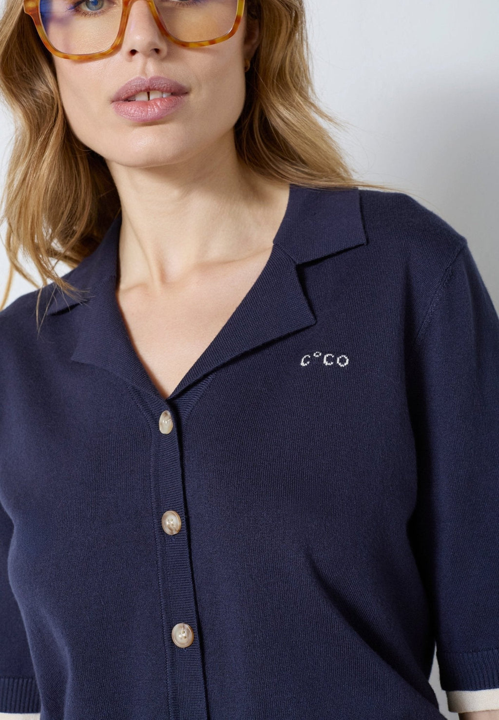 Co’Couture LueCC Crop Cardigan on lyhyt tummansininen neuletakki, jossa on kaulus, lyhyet hihat ja nappikiinnitys. Väljä malli sopii helposti kerrostamiseen.