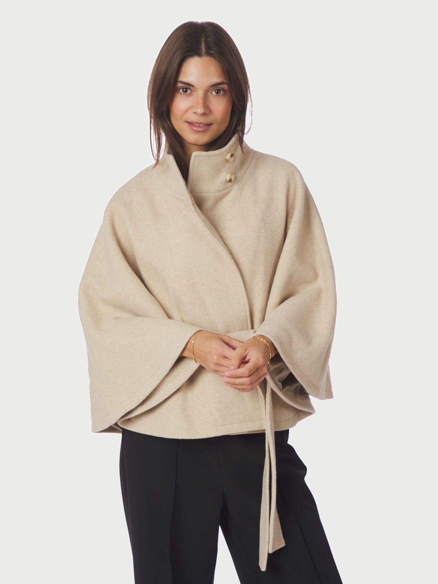 Neo Noir Cape Jacket on tyylikäs lyhyt villasekoitetakki viittamaisella leikkauksella. Korkea kaulus, vyötärövyö ja ajaton hiekan sävy viimeistelevät ilmeen.